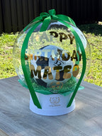 Clear snow globe with soccer ball and 'Happy Birthday' text, on a wooden surface with grass background - Lovy Details Miami